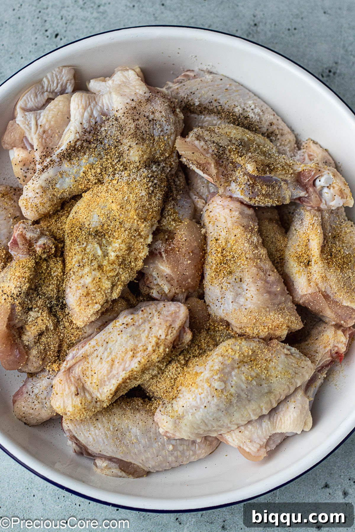 Raw chicken wings in a white bowl, freshly seasoned with a visible layer of powdered spices.
