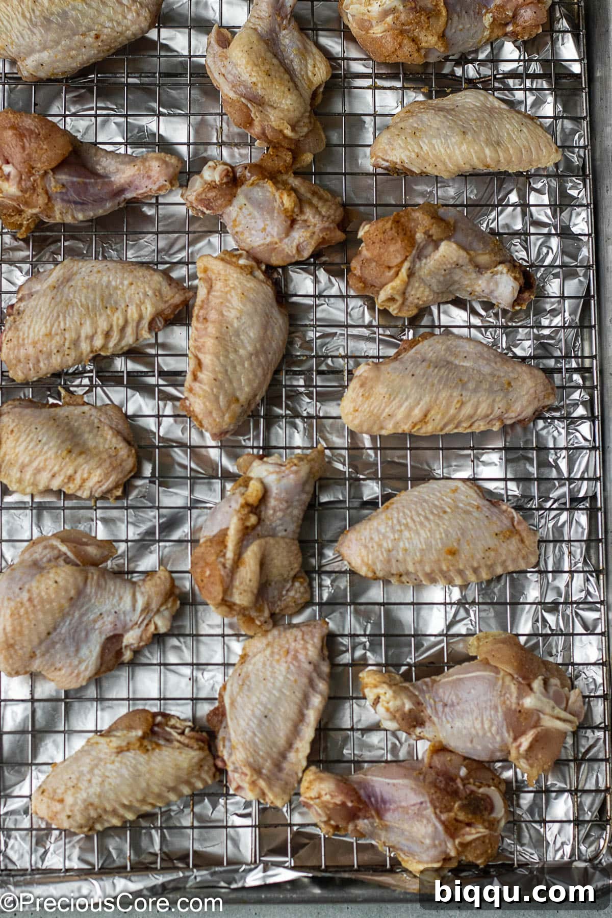 Raw, seasoned chicken wings meticulously arranged on a wire rack set over a baking sheet, ready for the oven.