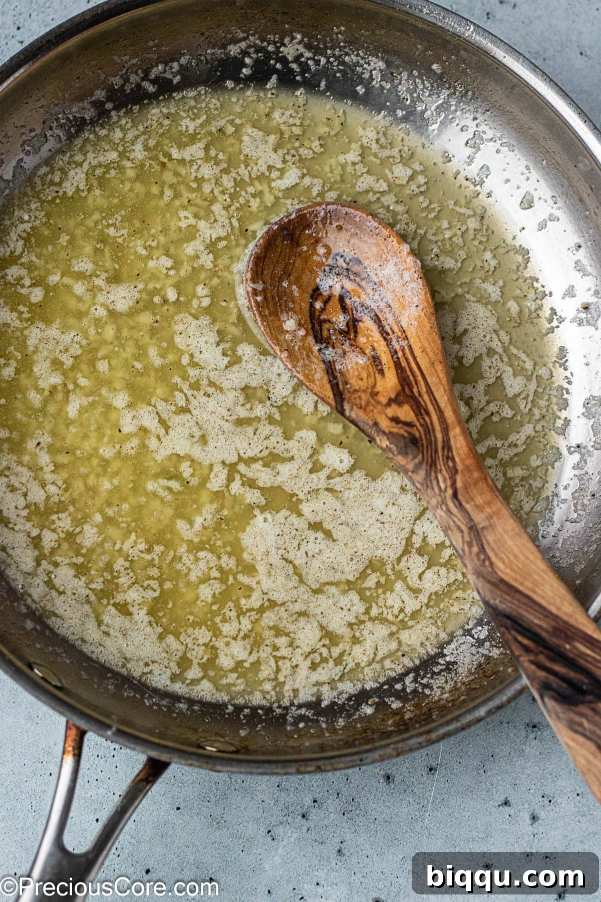 A stainless steel skillet holding a rich, golden garlic butter sauce with visible minced garlic pieces.