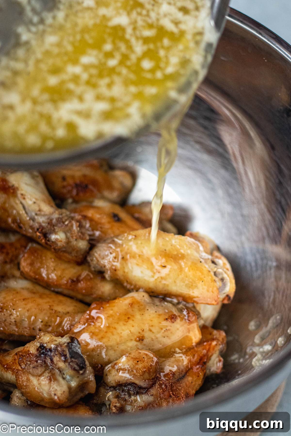 Rich garlic butter sauce being poured over a bowl of freshly cooked chicken wings, ready for tossing.