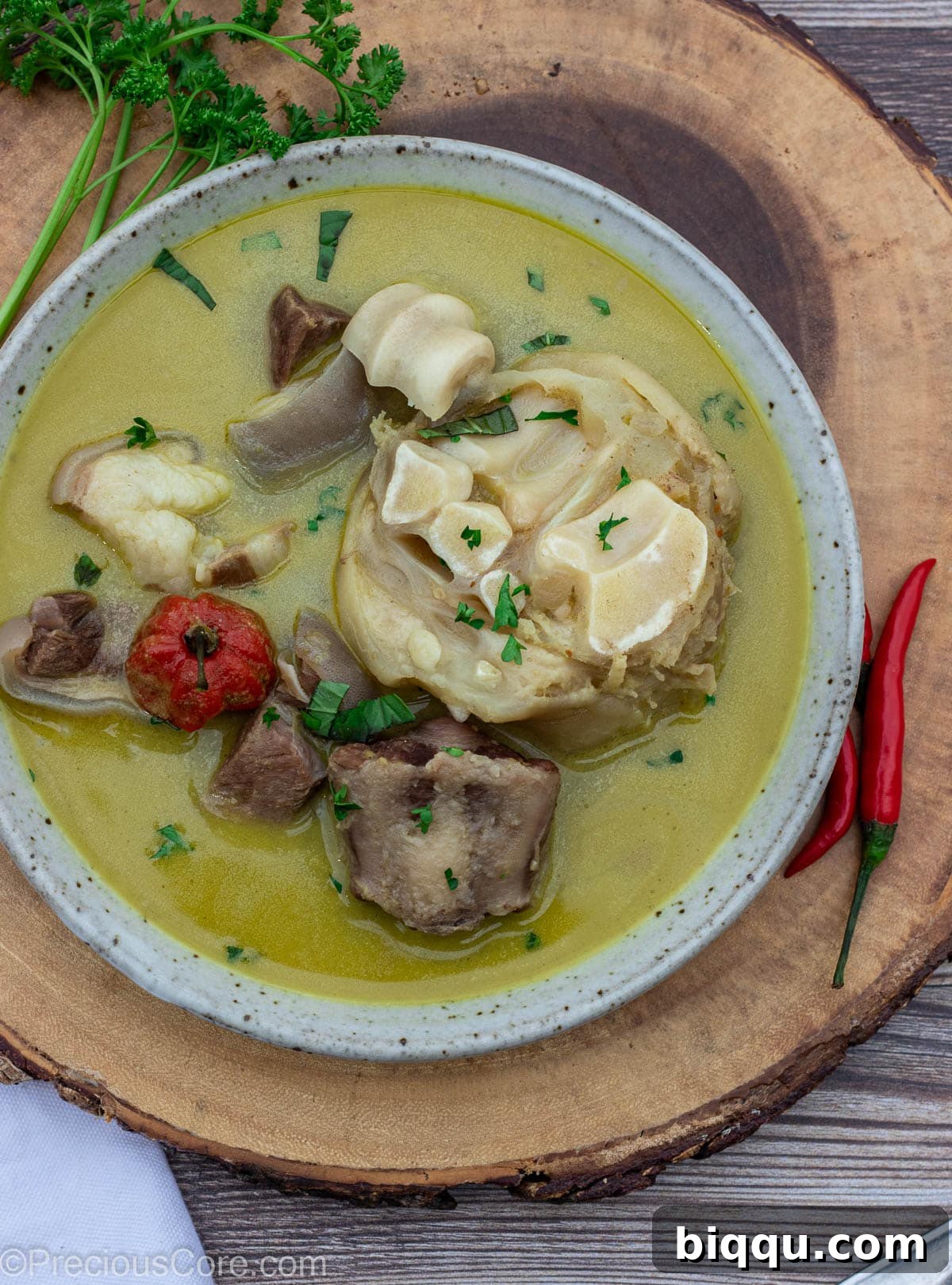 A hearty bowl of Cameroonian pepper soup, richly colored and garnished, sitting on a round platter.