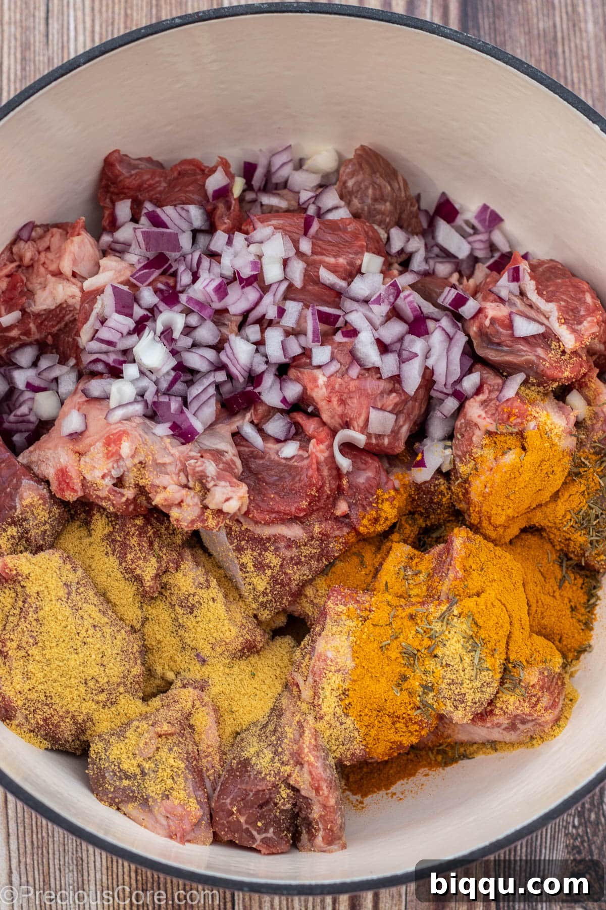Raw beef chunks with diced onions and seasoning powder in a pot, ready for boiling.