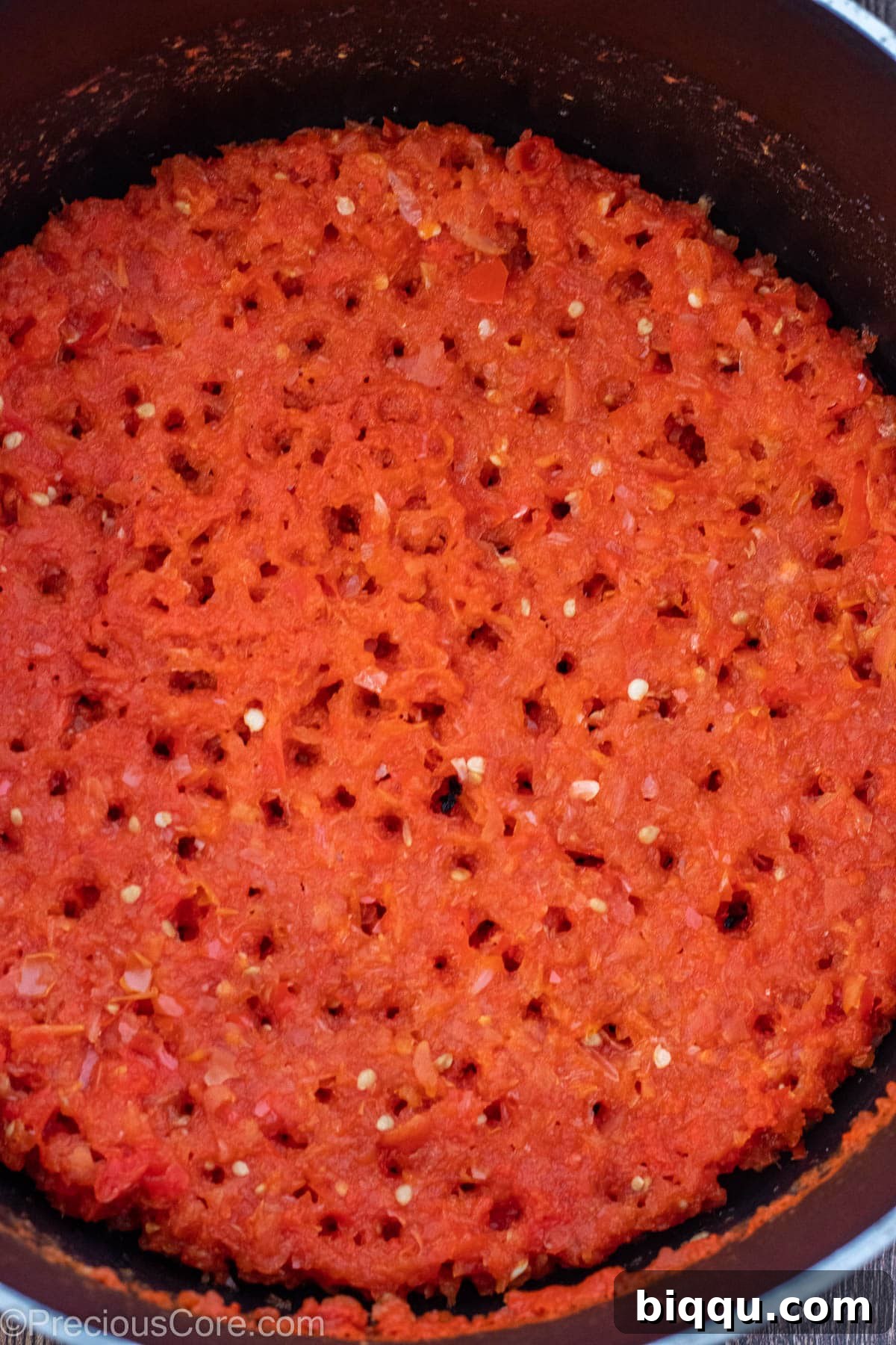 A pot of vibrant tomato-pepper-onion blend, simmering down until reduced.