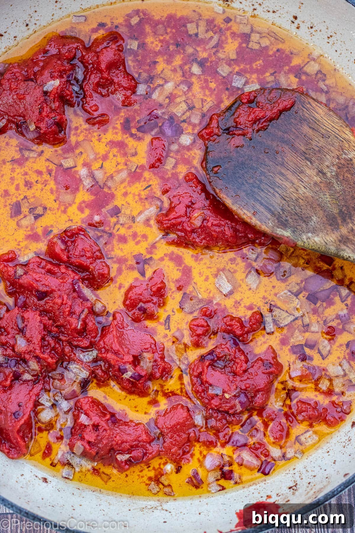 Diced onions and tomato paste cooking in oil in a pot.