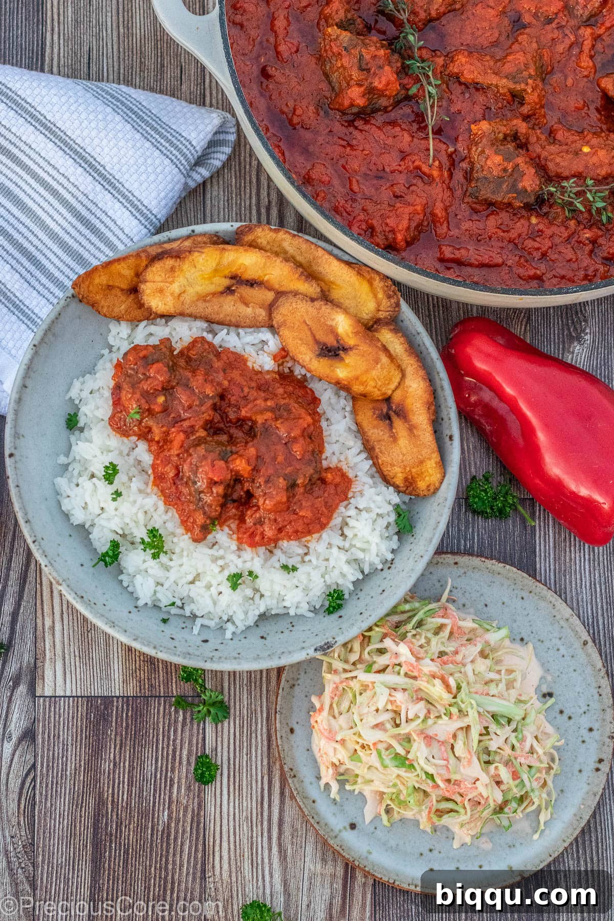 Nigerian beef stew elegantly served with a side of white rice, sweet fried plantains, and fresh coleslaw, creating a complete and balanced meal.