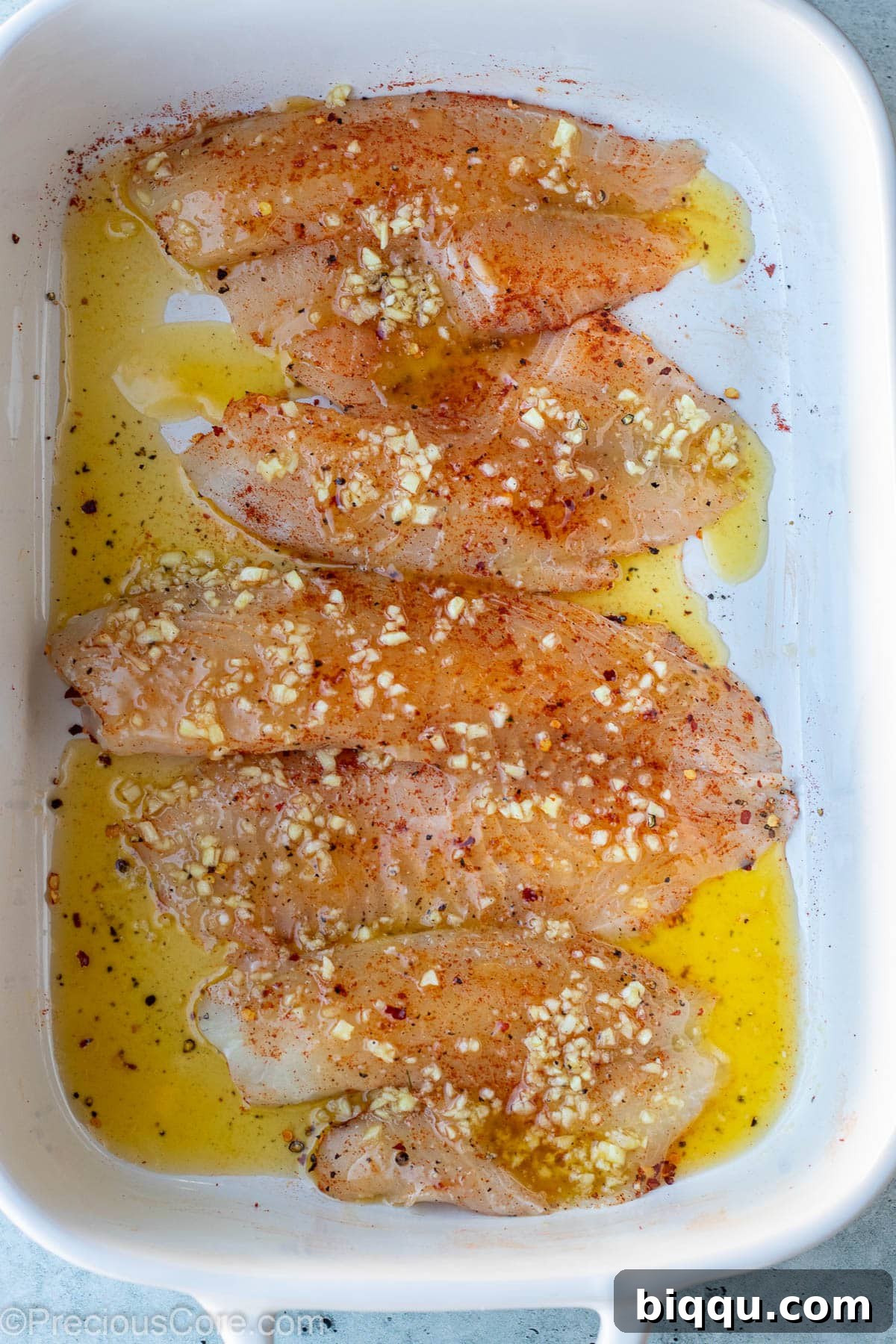 Raw tilapia fillets completely covered and glistening with the luscious garlic butter sauce, perfectly prepared and ready for baking.