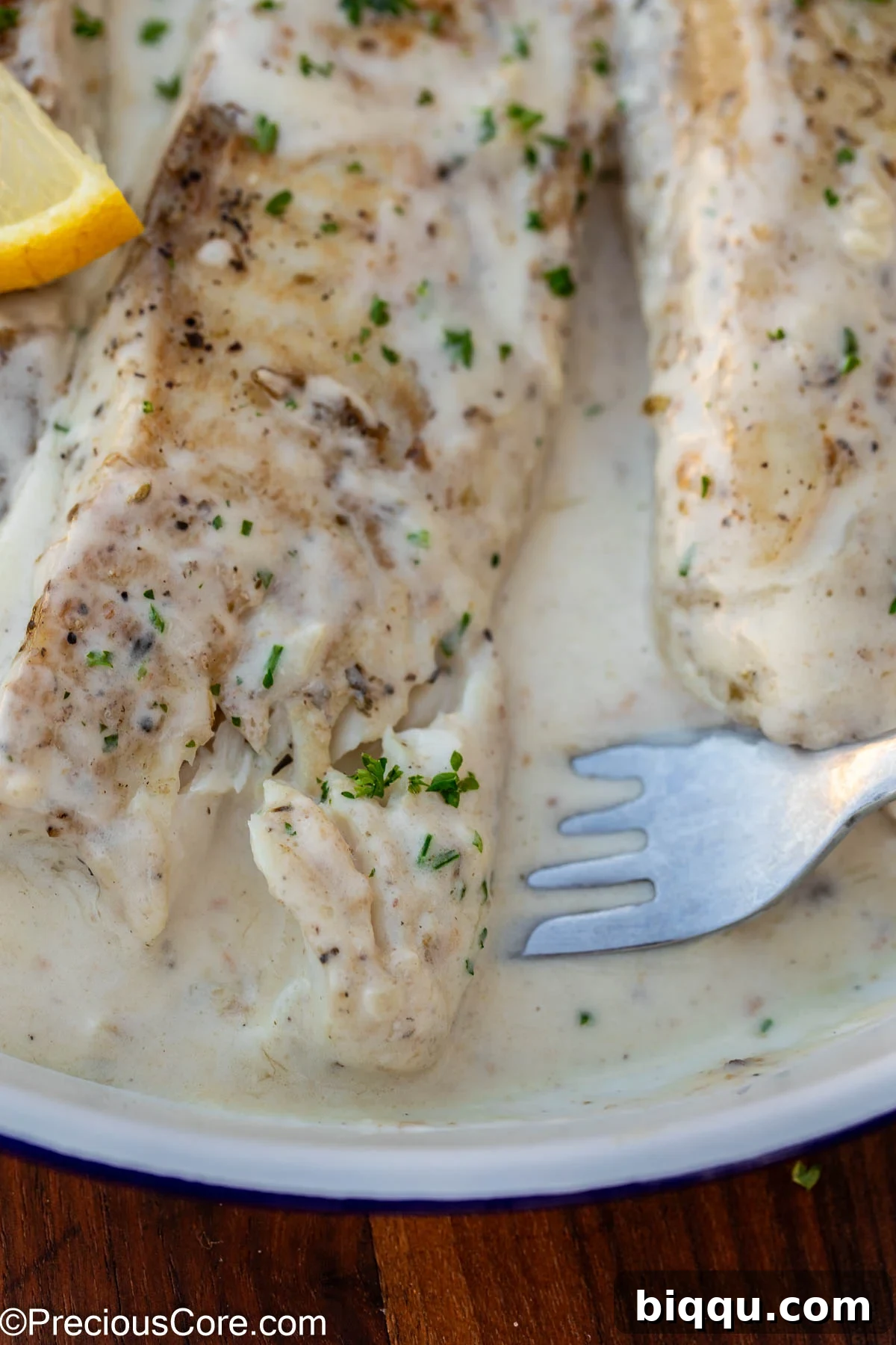 Silken Fish Delight 3 A fork lifts a piece of flaky fish from a pan filled with creamy white sauce, highlighting its tender texture.