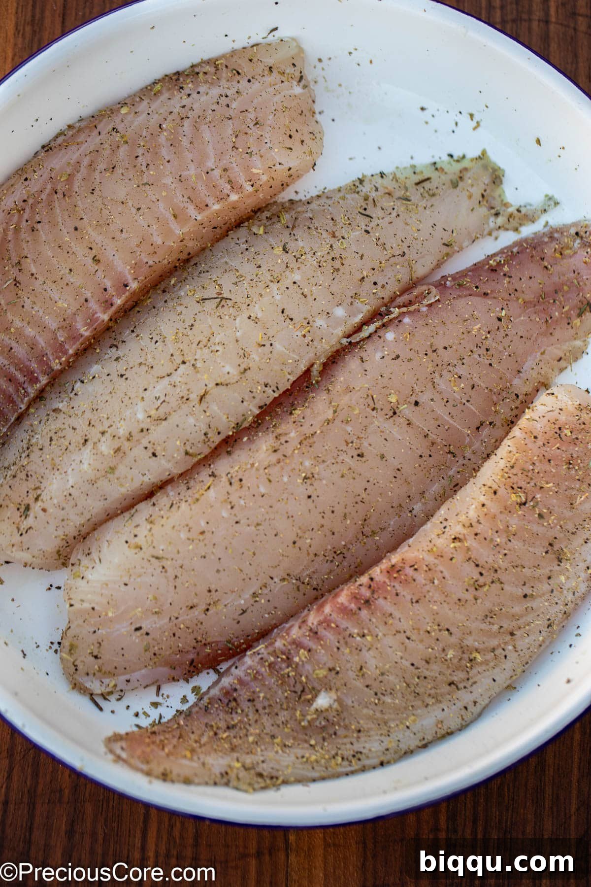 Silken Fish Delight 5 Raw tilapia fillets seasoned with salt, pepper, and Italian seasoning, ready for cooking.