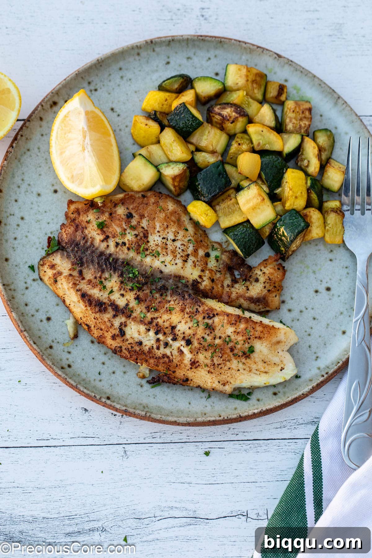 Lemon pepper tilapia on a plate with sautéed zucchini.