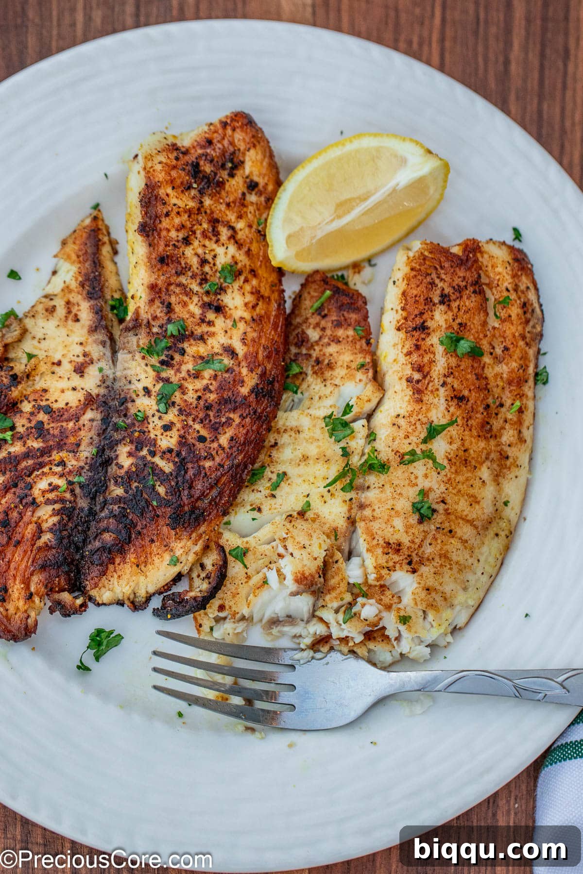 2 lemon pepper tilapia fillets on a white plate.