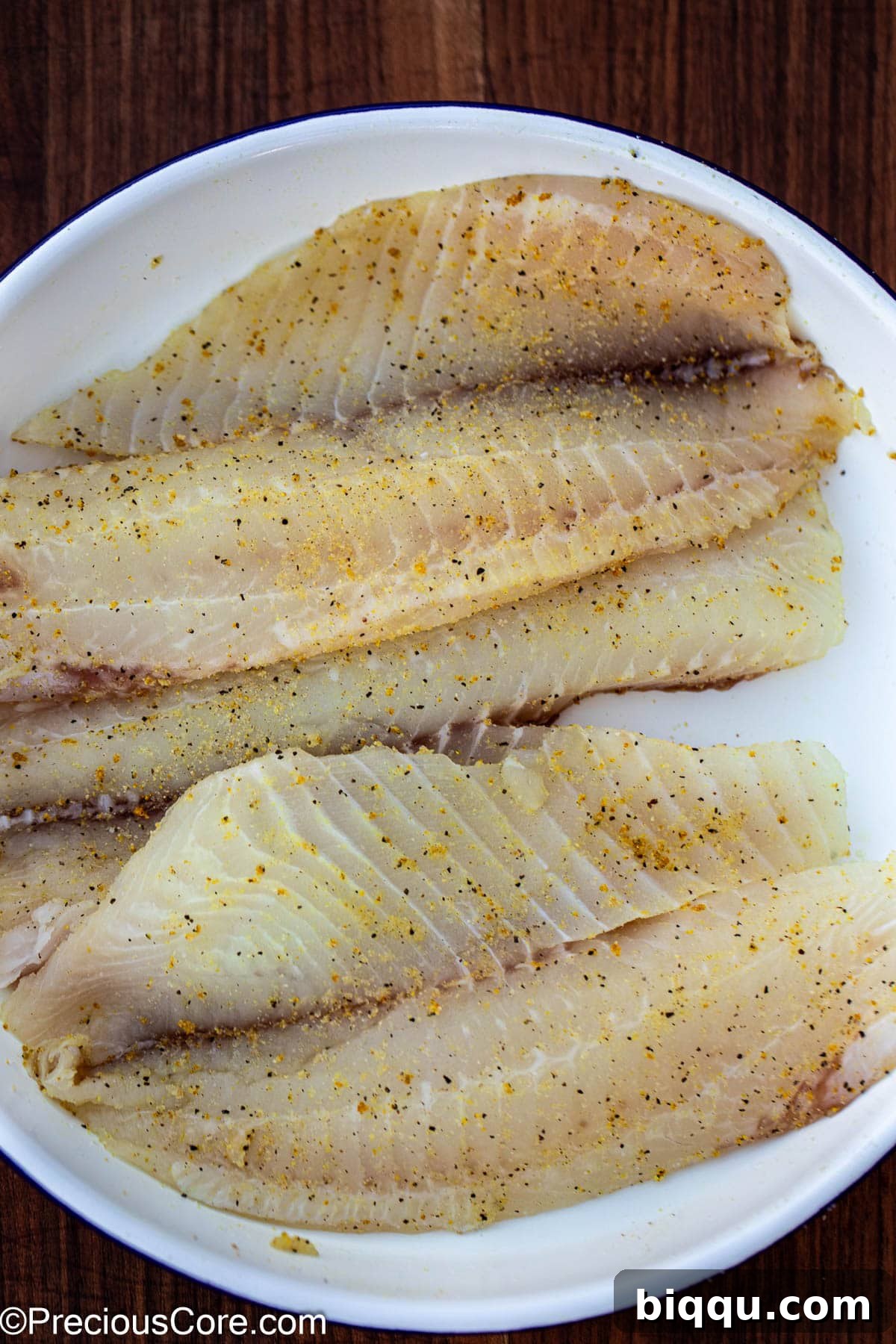 Seasoned tilapia fillets in a white bowl.