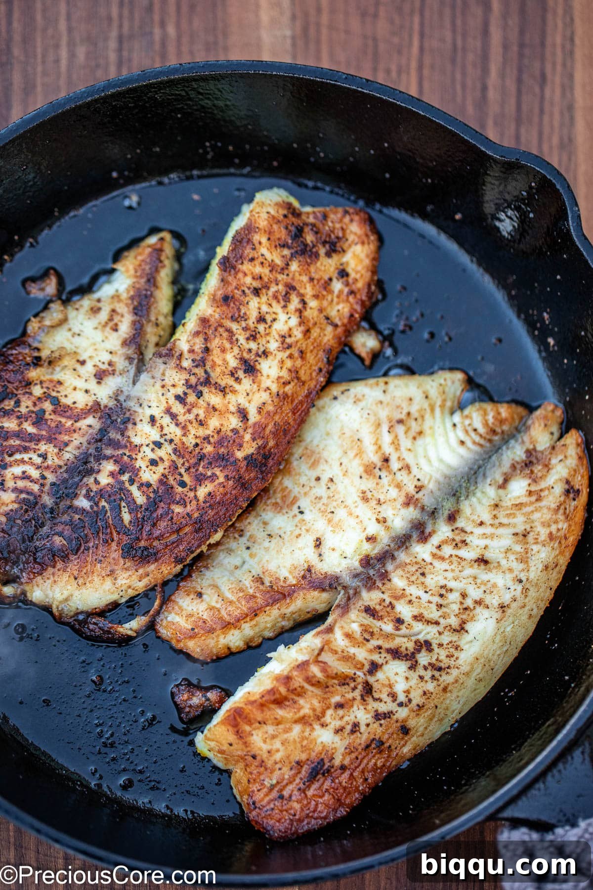 2 cooked fish fillets in a cast iron skillet.
