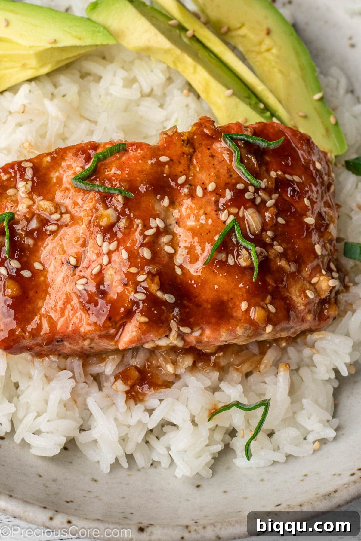 Teriyaki Salmon over rice with avocado slices in a bowl, garnished with sesame seeds.