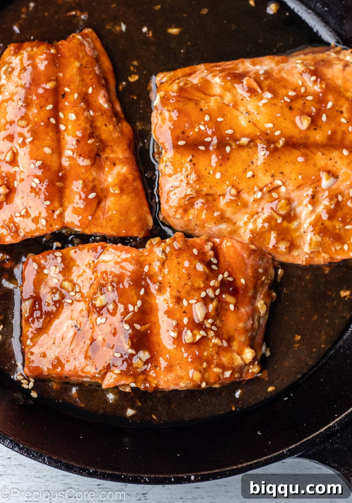 Pan fried teriyaki salmon in a cast iron skillet, coated with glossy sauce.