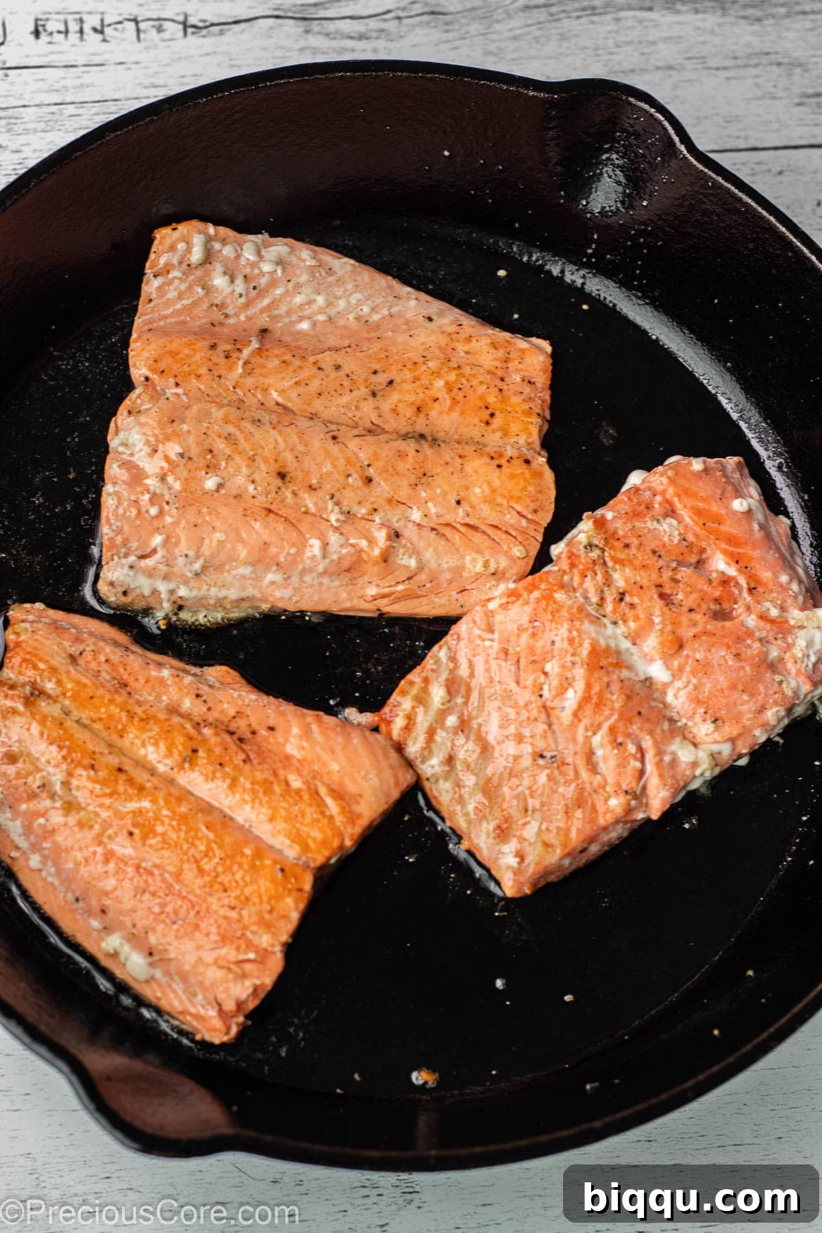 Salmon fillets pan-frying in a skillet, getting a golden crust.