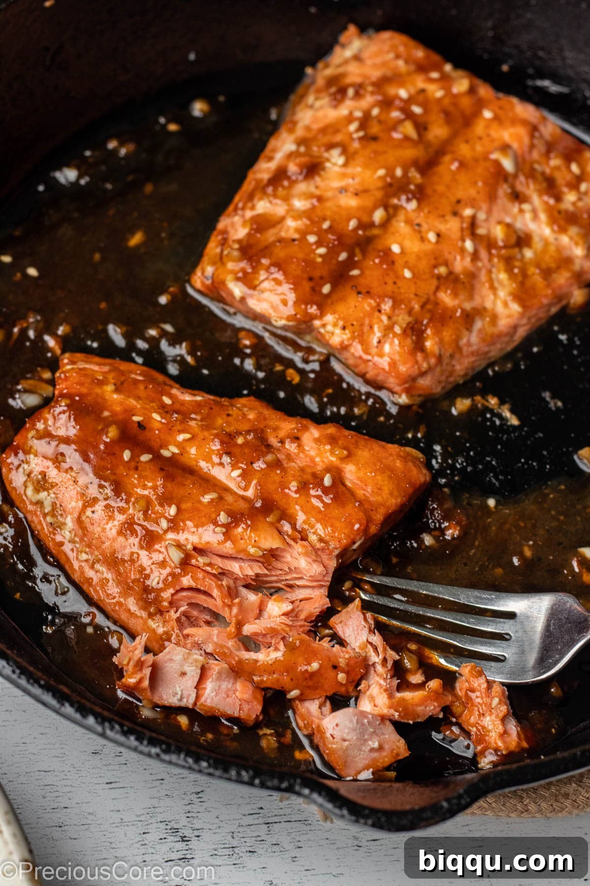 Two salmon fillets in a pan, one flaked with a fork to show perfect doneness.