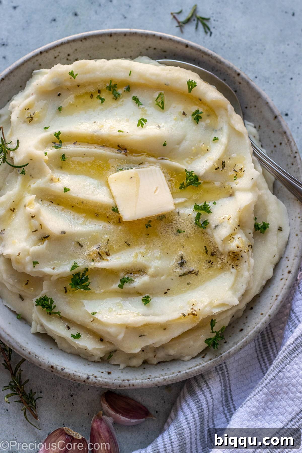 A beautifully presented bowl of creamy Rosemary Garlic Mashed Potatoes, generously topped with melted butter and a sprinkle of fresh parsley, ready to be served.