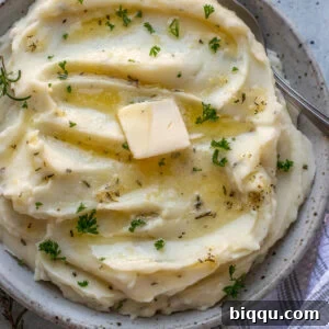 A square image of a serving bowl filled with creamy Rosemary Garlic Mashed Potatoes, garnished with fresh herbs.