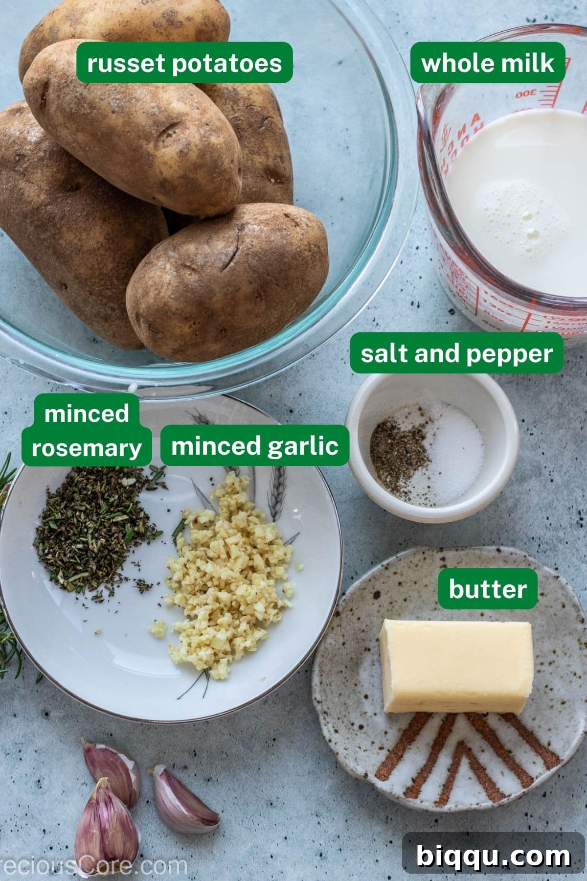 A beautifully arranged flat lay of fresh ingredients including russet potatoes, a jug of whole milk, minced garlic, fresh rosemary sprigs, salt, pepper, and a stick of unsalted butter.