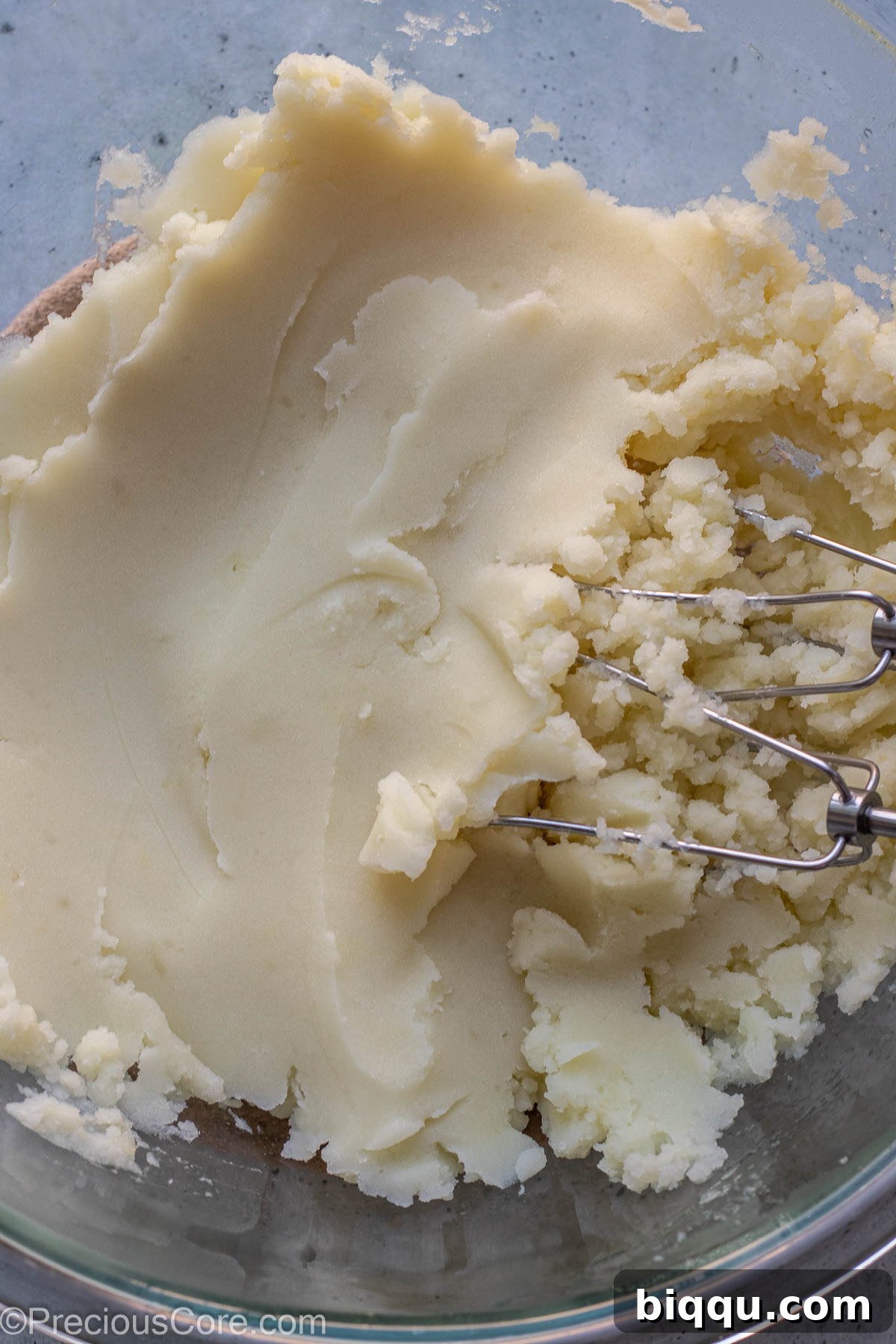 A hand beater expertly combining the mashed potatoes in a large mixing bowl to achieve a smooth, lump-free consistency.