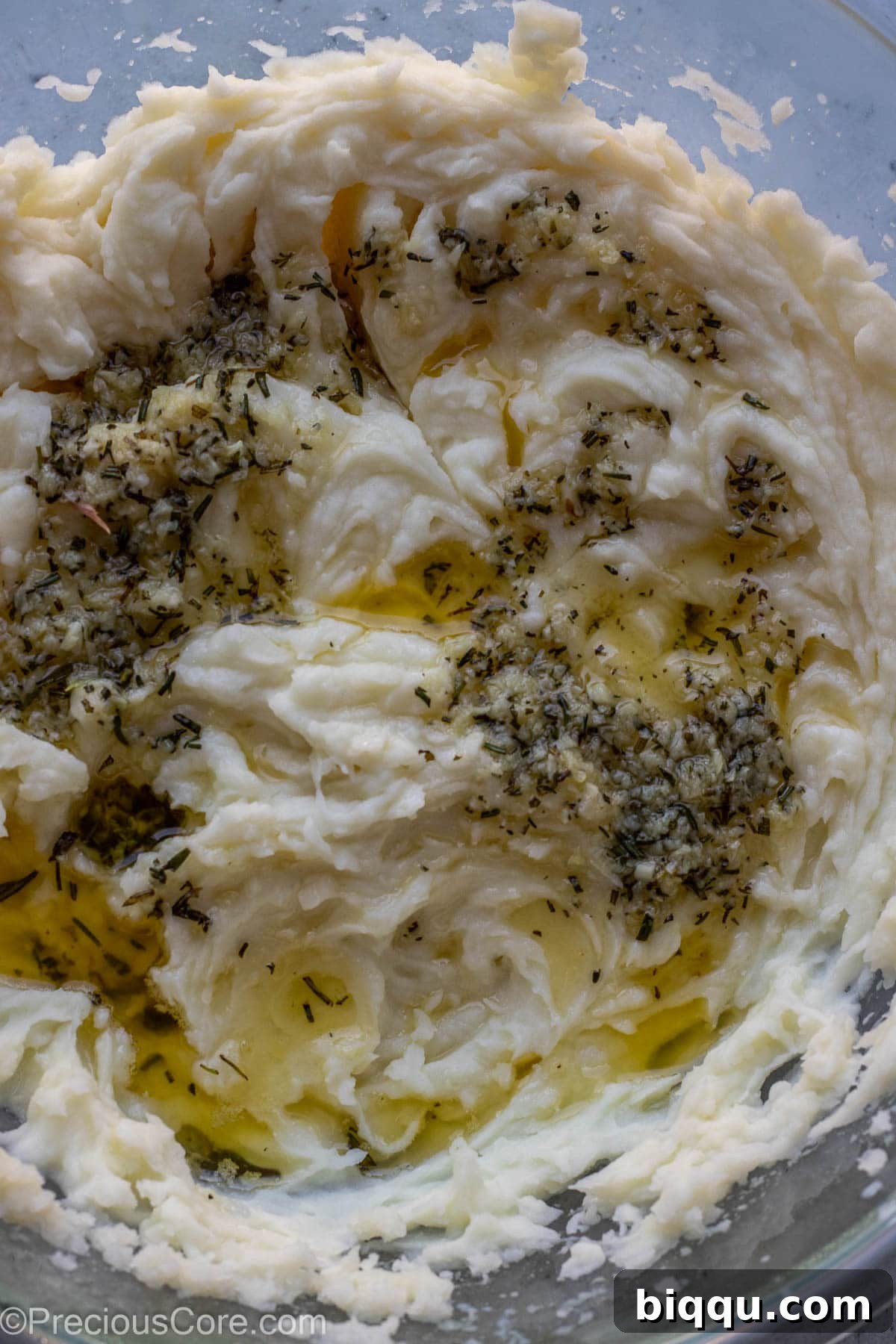 Fragrant melted butter infused with minced garlic and fresh rosemary being poured over a bowl of hot mashed potatoes.