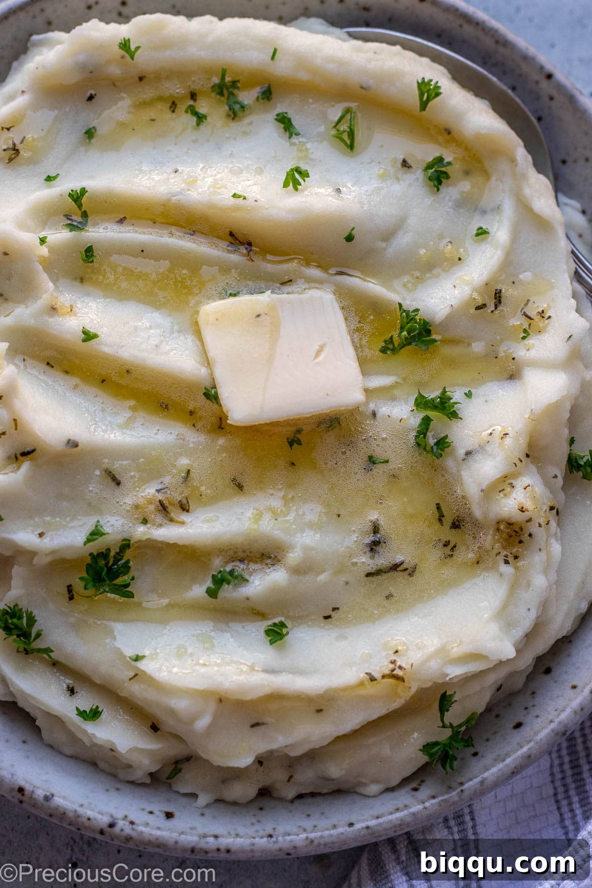 A close-up shot of incredibly creamy mashed potatoes in a serving bowl, highlighting their rich texture and garnished appearance.