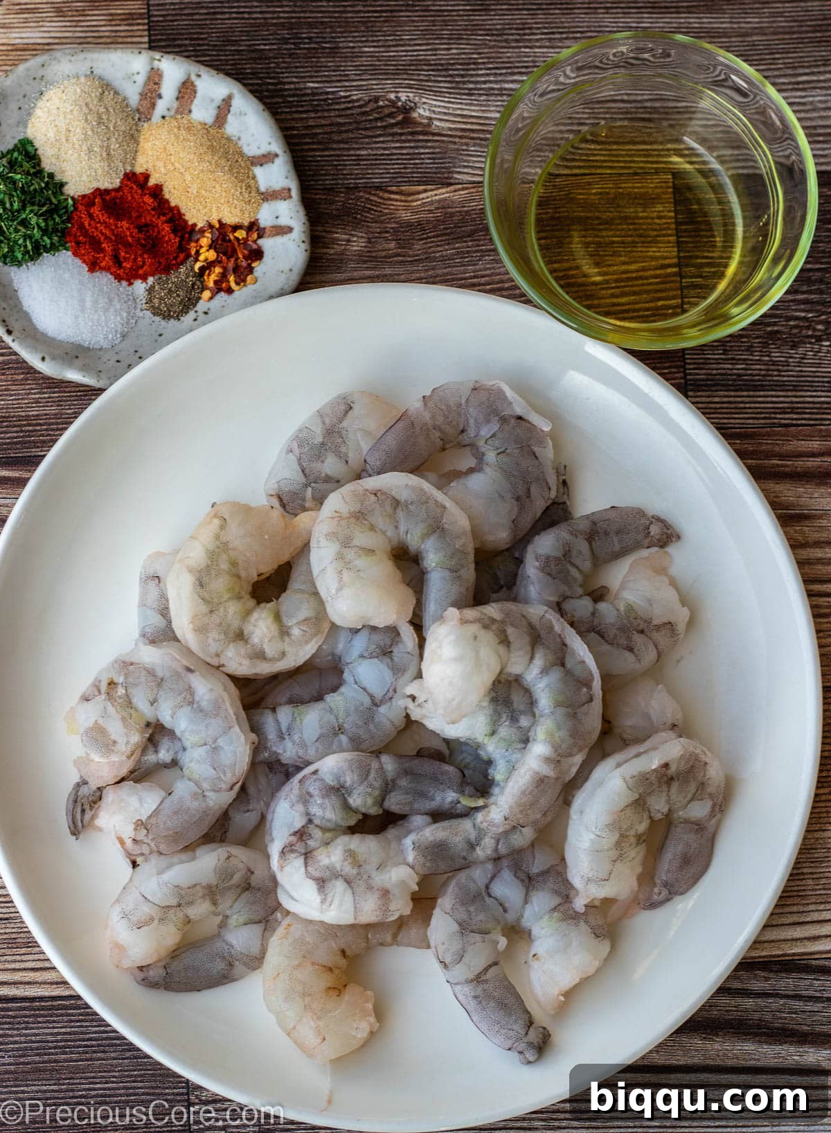 A visual guide to raw shrimp, a selection of dry seasonings, and a small bowl of olive oil, ready for pan-searing.