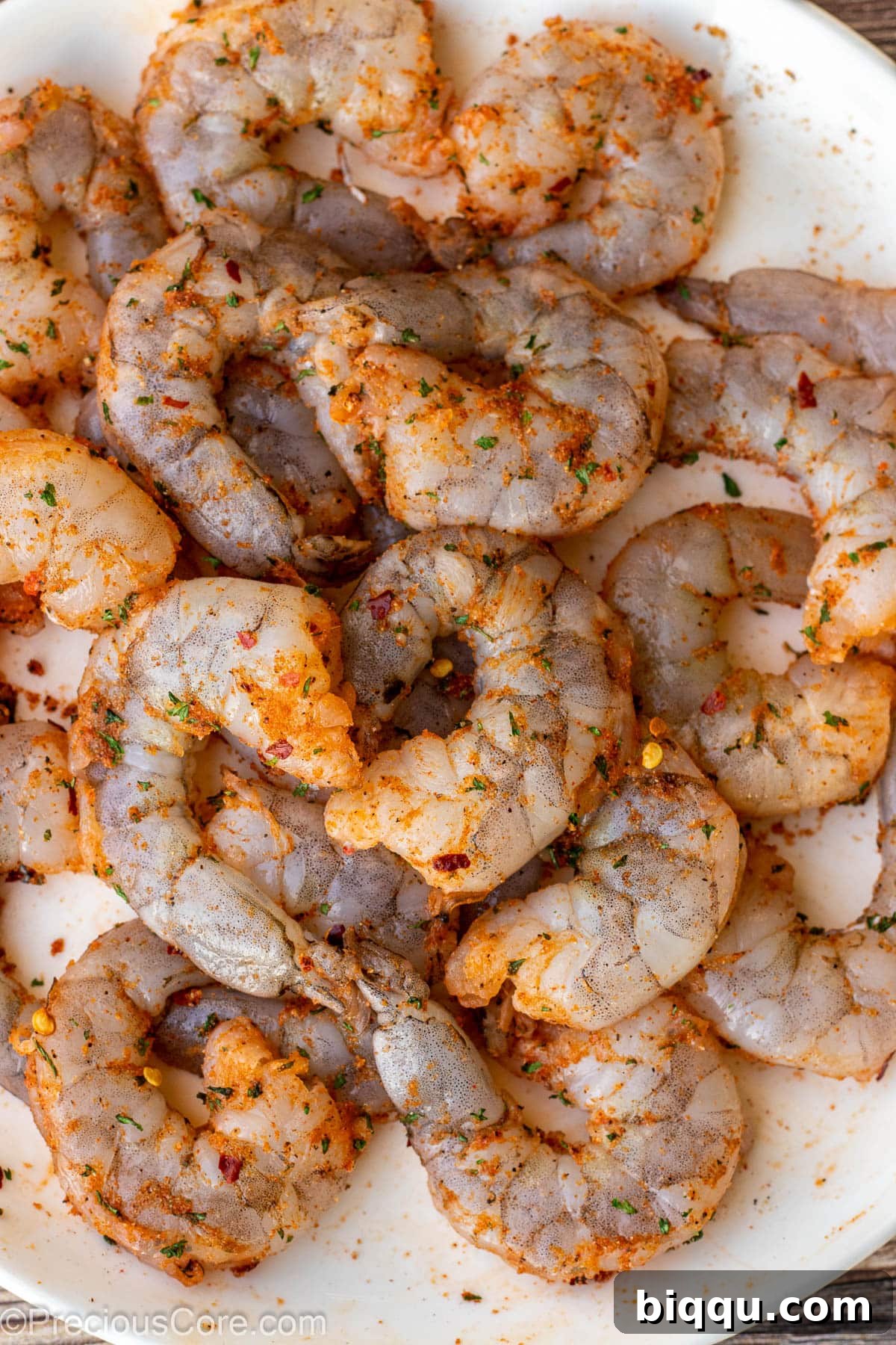 Raw shrimp meticulously seasoned with a vibrant mix of spices, awaiting its transformation on a clean white plate.
