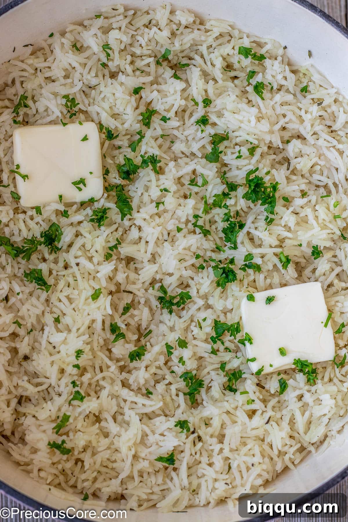 The ultimate finishing touch: perfectly cooked garlic herb rice crowned with generous pats of melting unsalted butter and a vibrant sprinkle of fresh minced parsley, ready to be fluffed and served.