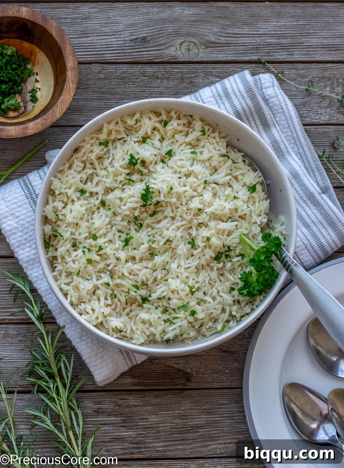 A charming scene featuring a bowl of perfectly seasoned garlic herb rice, garnished with fresh herbs, positioned next to a stack of pristine white plates, poised for a delightful meal.