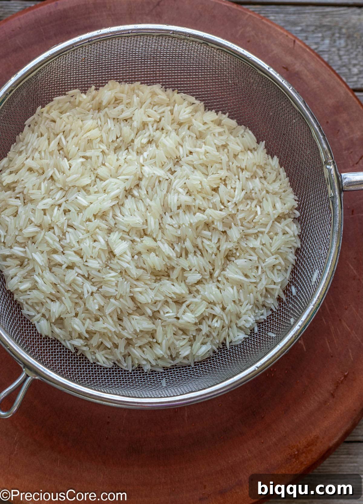 Fluffy Basmati rice being rinsed thoroughly in a fine mesh strainer under cold running water, with the clear runoff indicating successful removal of excess starch.