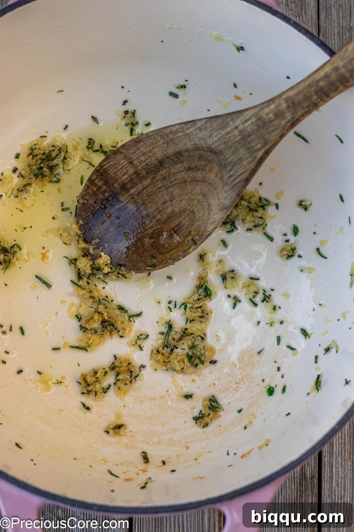 Minced garlic and fresh sprigs of rosemary and thyme gently sizzling in olive oil within a sturdy cast iron enamel pot, releasing their captivating aromatic essence, forming the base of the flavorful rice.