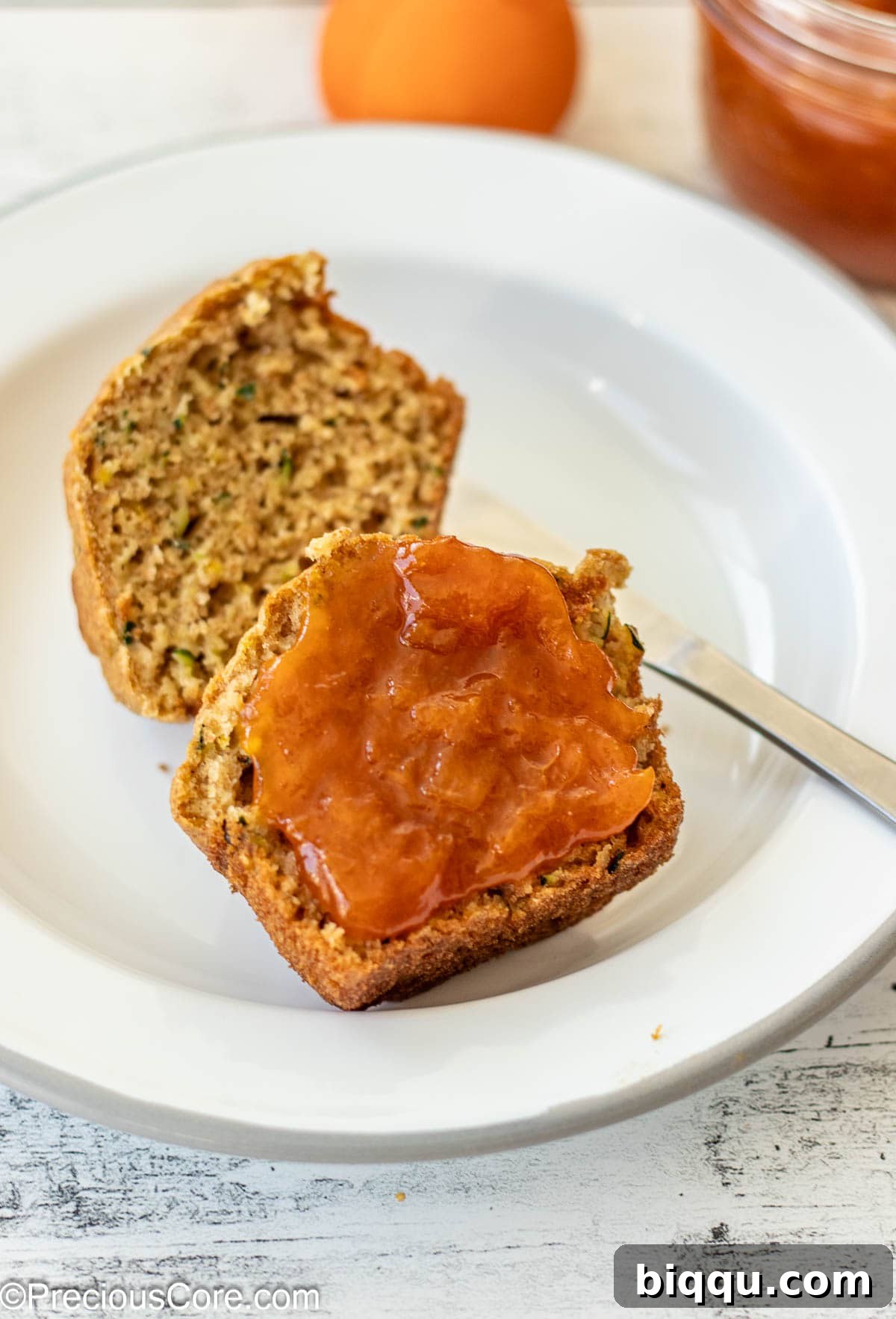 A zucchini muffin with apricot preserves spread on one half.
