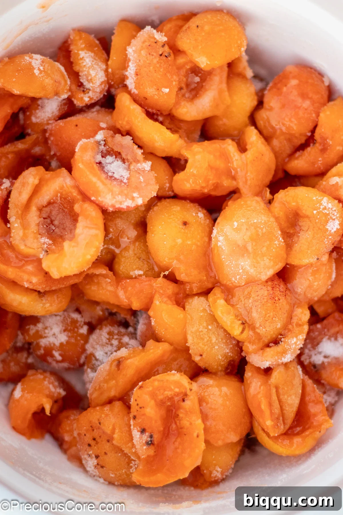 Halved apricots mixed with granulated sugar in a white bowl.
