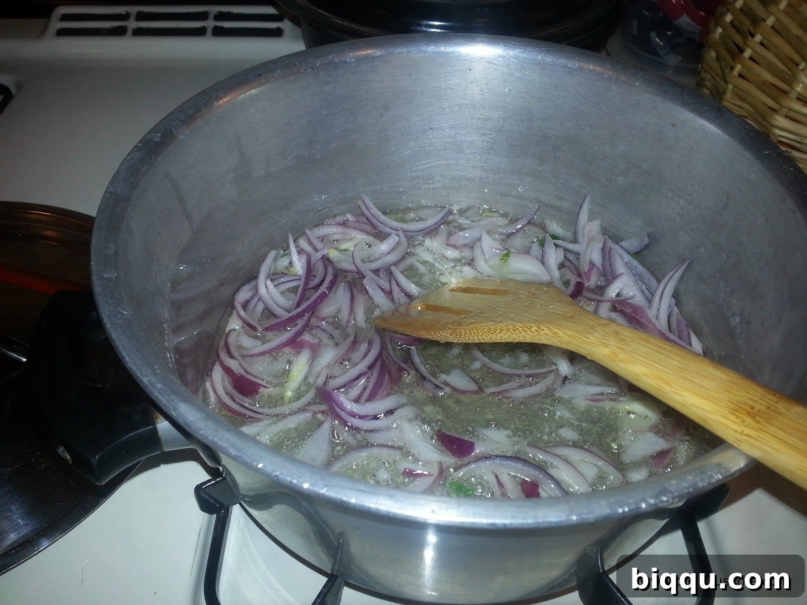 Onions sizzling in hot oil in a pot, beginning to turn translucent.