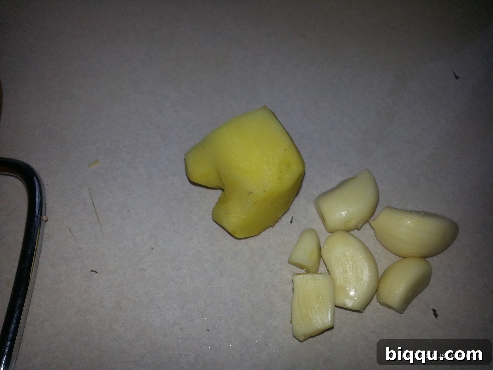 Fresh garlic cloves and a piece of ginger, peeled and ready for grating or blending.