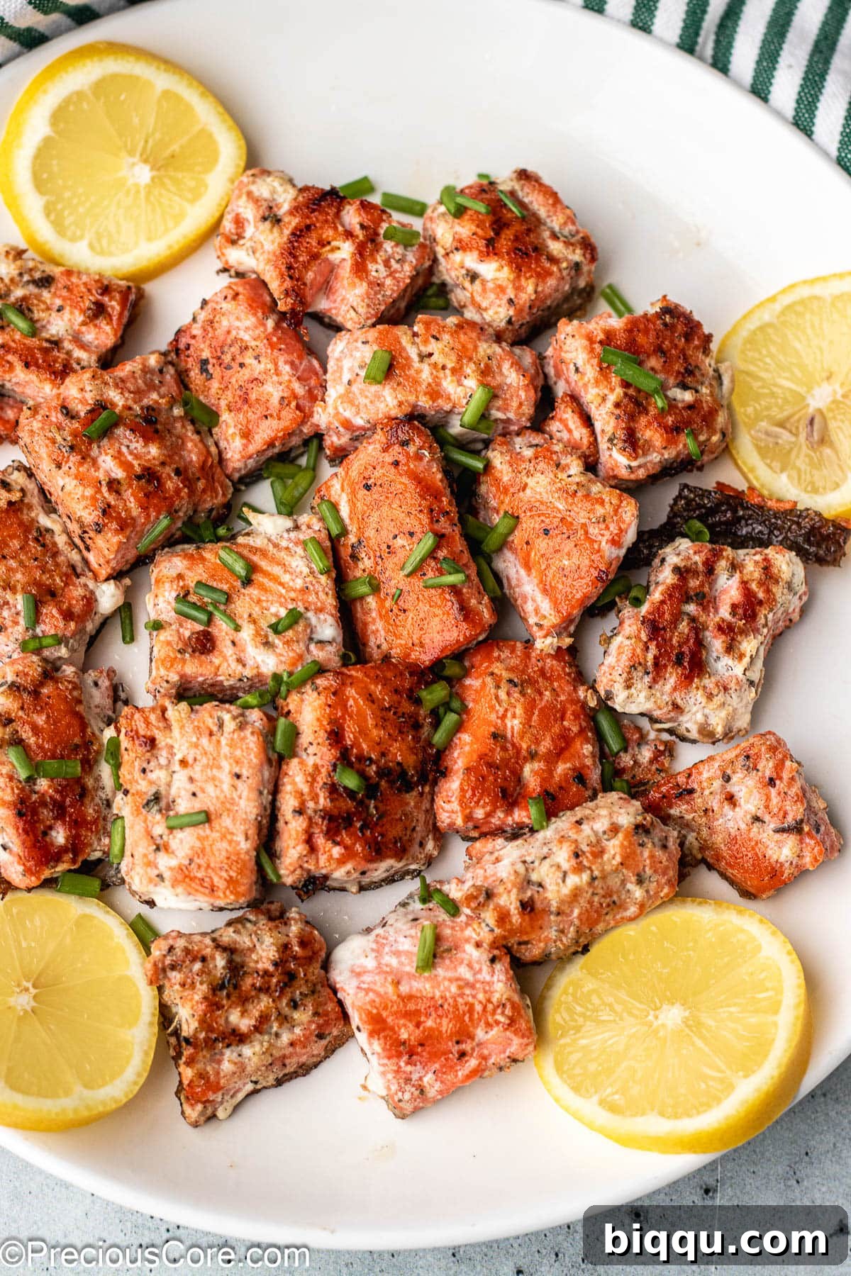 Delicious Salmon Bites 8 Perfectly seared salmon bites on a white plate, elegantly garnished with fresh lemon slices and dill.