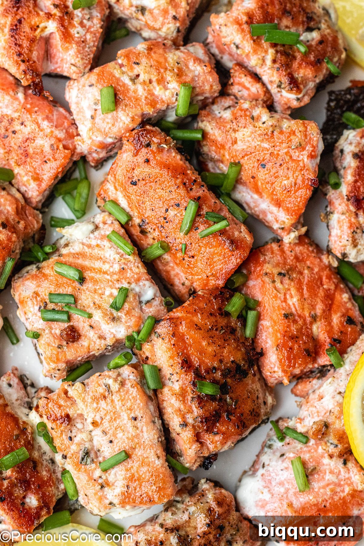 About 1-inch sized salmon bites on a white plate, garnished with fresh herbs.