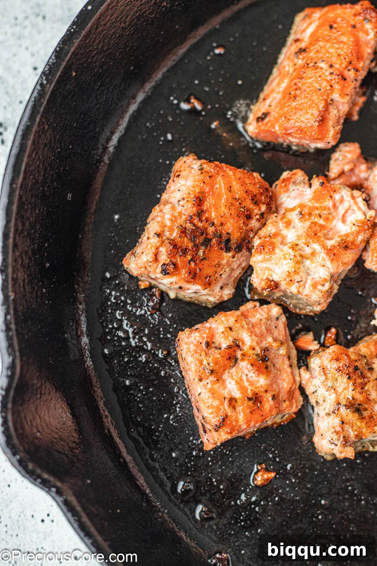 Delicious Salmon Bites 3 Seasoned salmon cubes sizzling in a hot cast iron skillet, cooking to perfection.