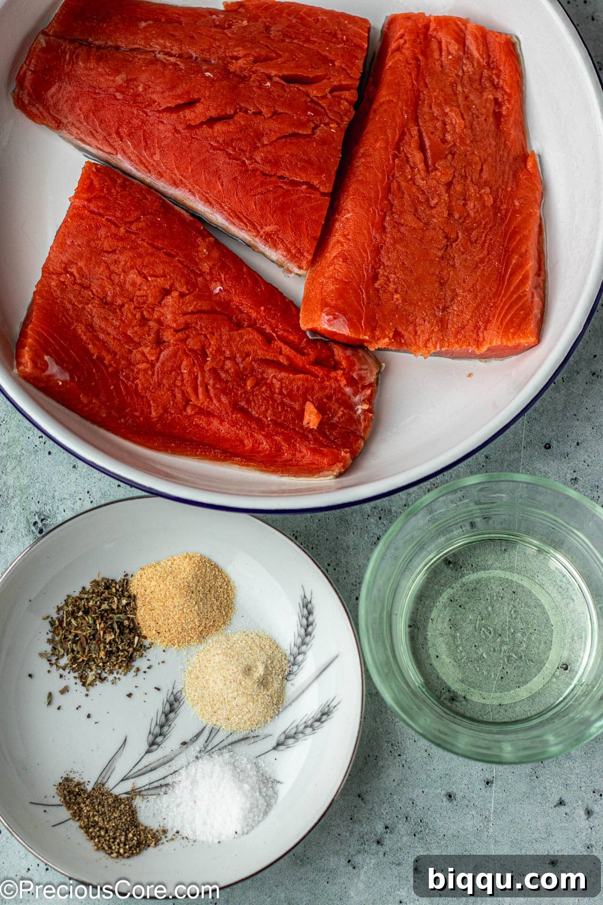 Delicious Salmon Bites 4 Fresh salmon fillet, a bottle of olive oil, and a small bowl of mixed seasonings on a wooden board.
