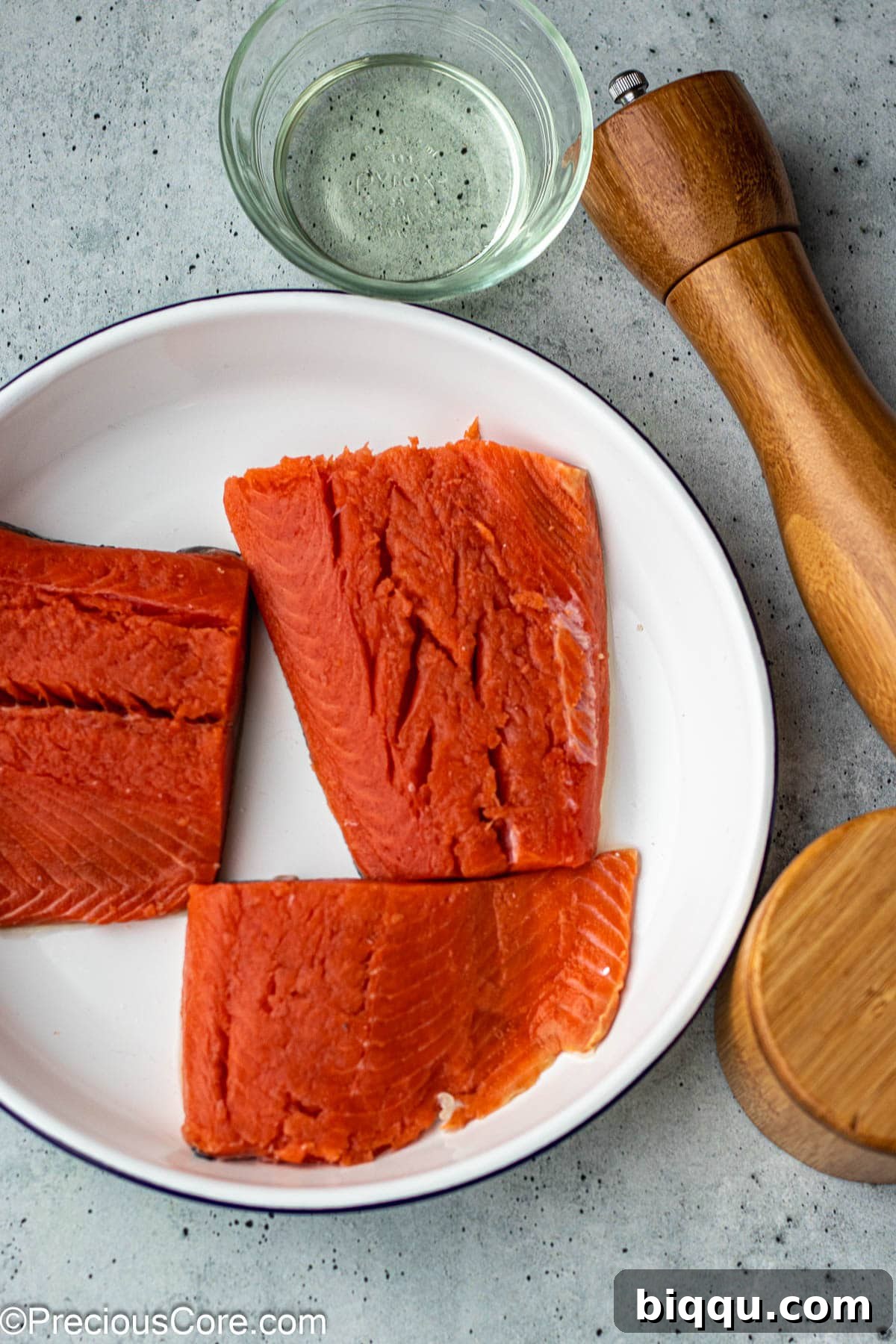 Fresh sockeye salmon fillet, coarse sea salt, freshly ground black pepper, and high-quality olive oil are the core ingredients laid out.