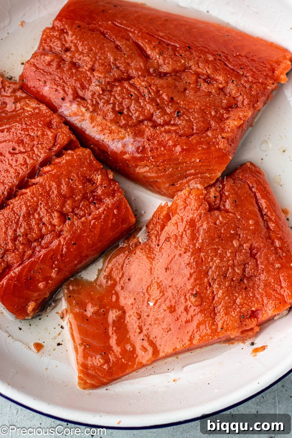 Sockeye salmon fillets generously seasoned with olive oil, salt, and pepper, resting in a white bowl, ready for grilling.