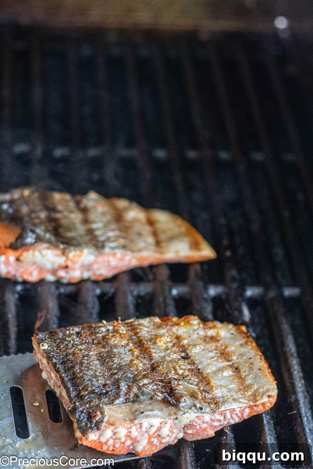 Skin-on sockeye salmon fillets cooking on a hot grill, showing perfect sear marks developing on the surface.
