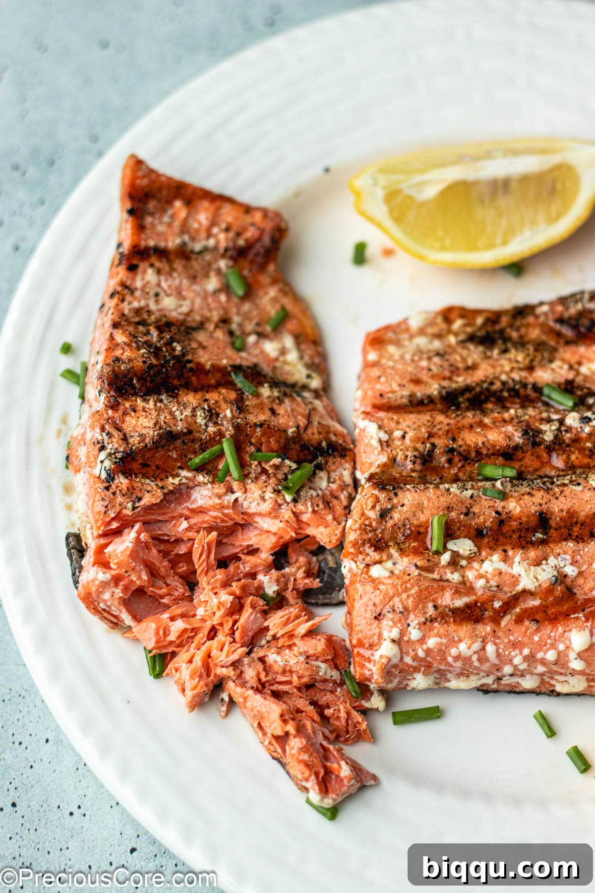 Two grilled salmon fillets on a white plate, one showing a fork gently flaking the perfectly cooked flesh, indicating ideal doneness.