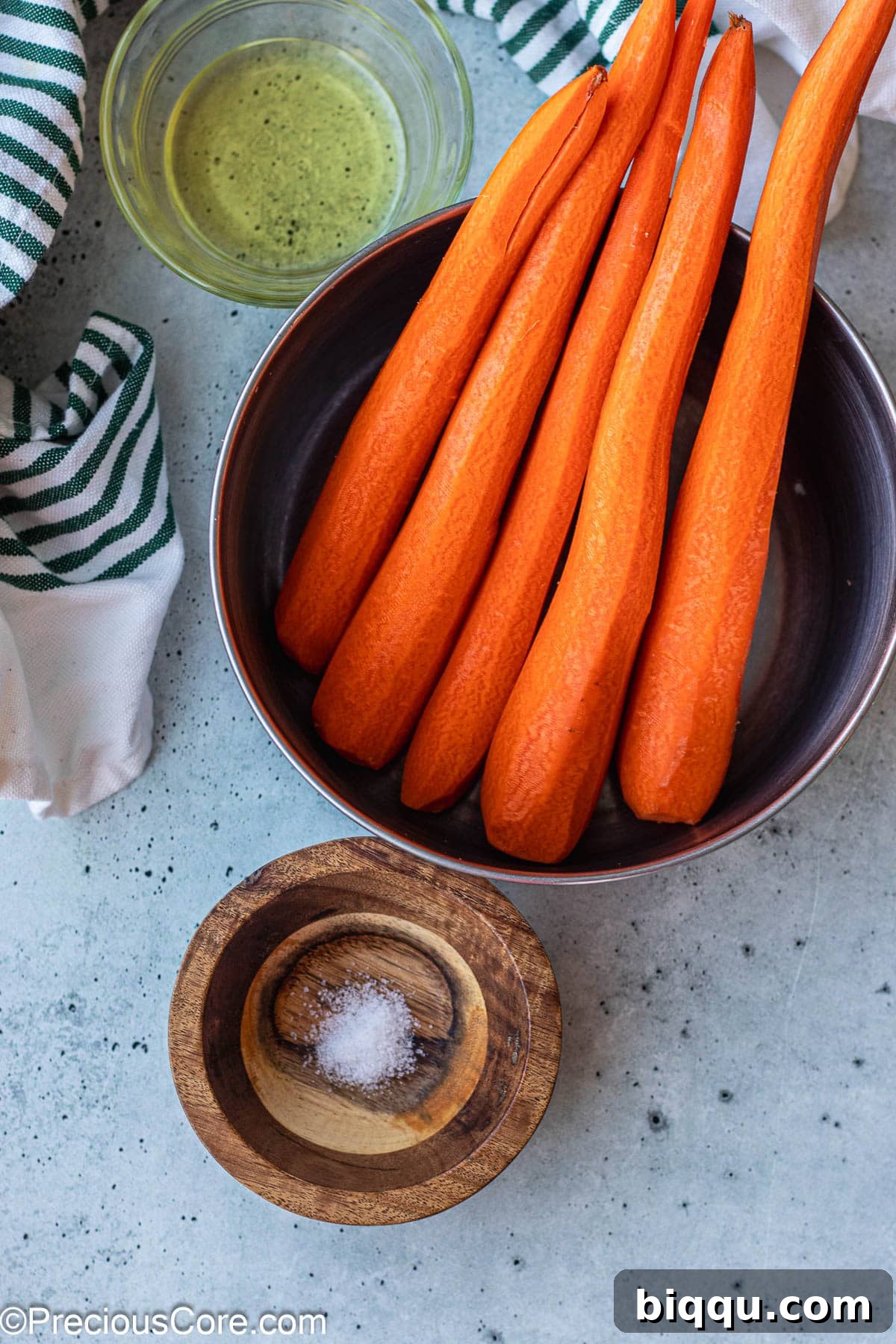 Fresh organic carrots, a bottle of olive oil, and a small bowl of sea salt, the three simple ingredients for fried carrots.