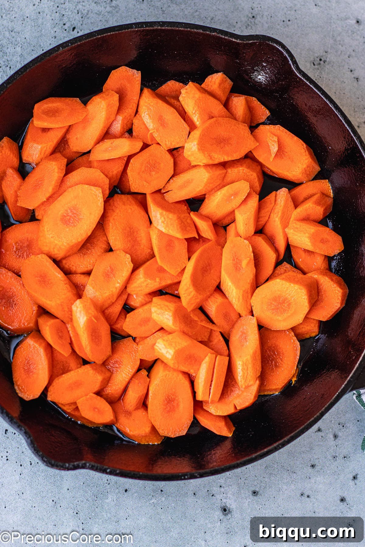 Carrot slices sizzling and caramelizing in a hot cast iron skillet.