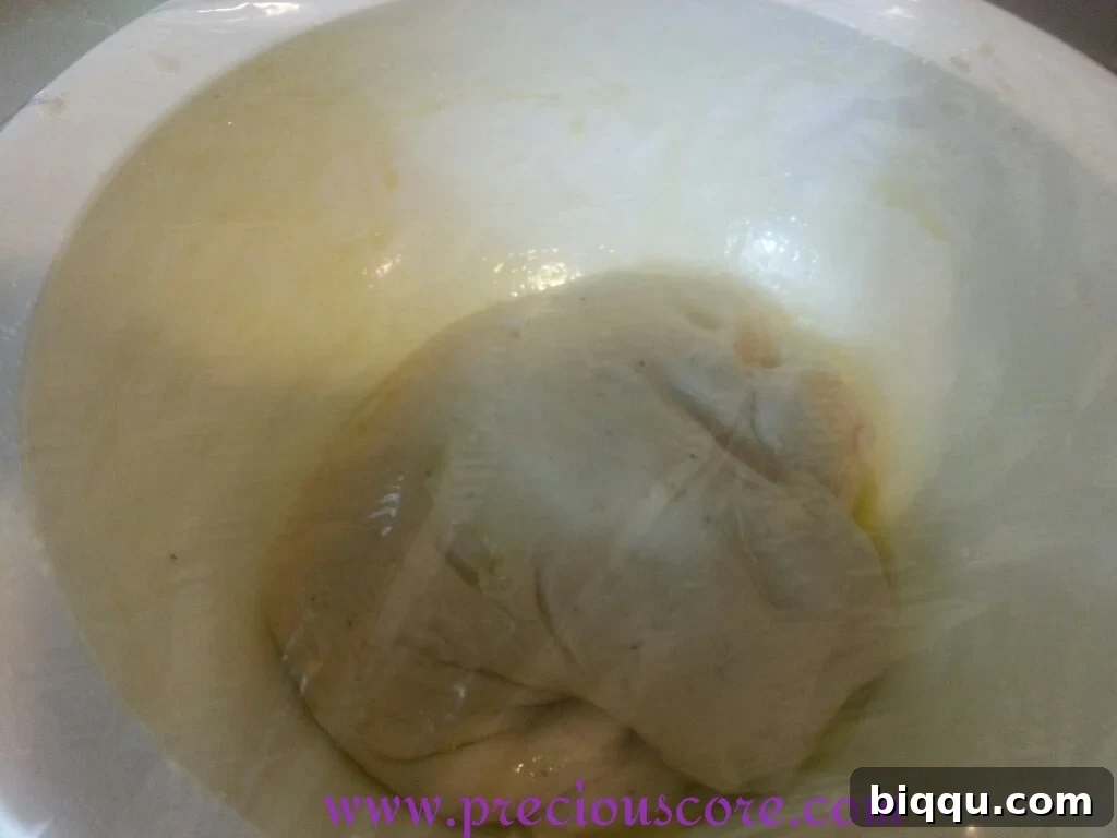 Bowl of dough covered with a kitchen towel over plastic wrap for insulation