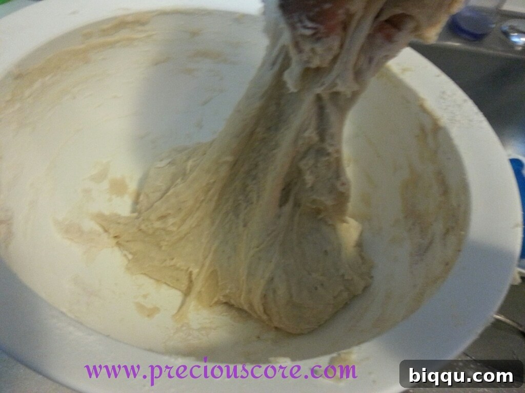 Soft, elastic bread dough forming in a mixing bowl, slightly sticky