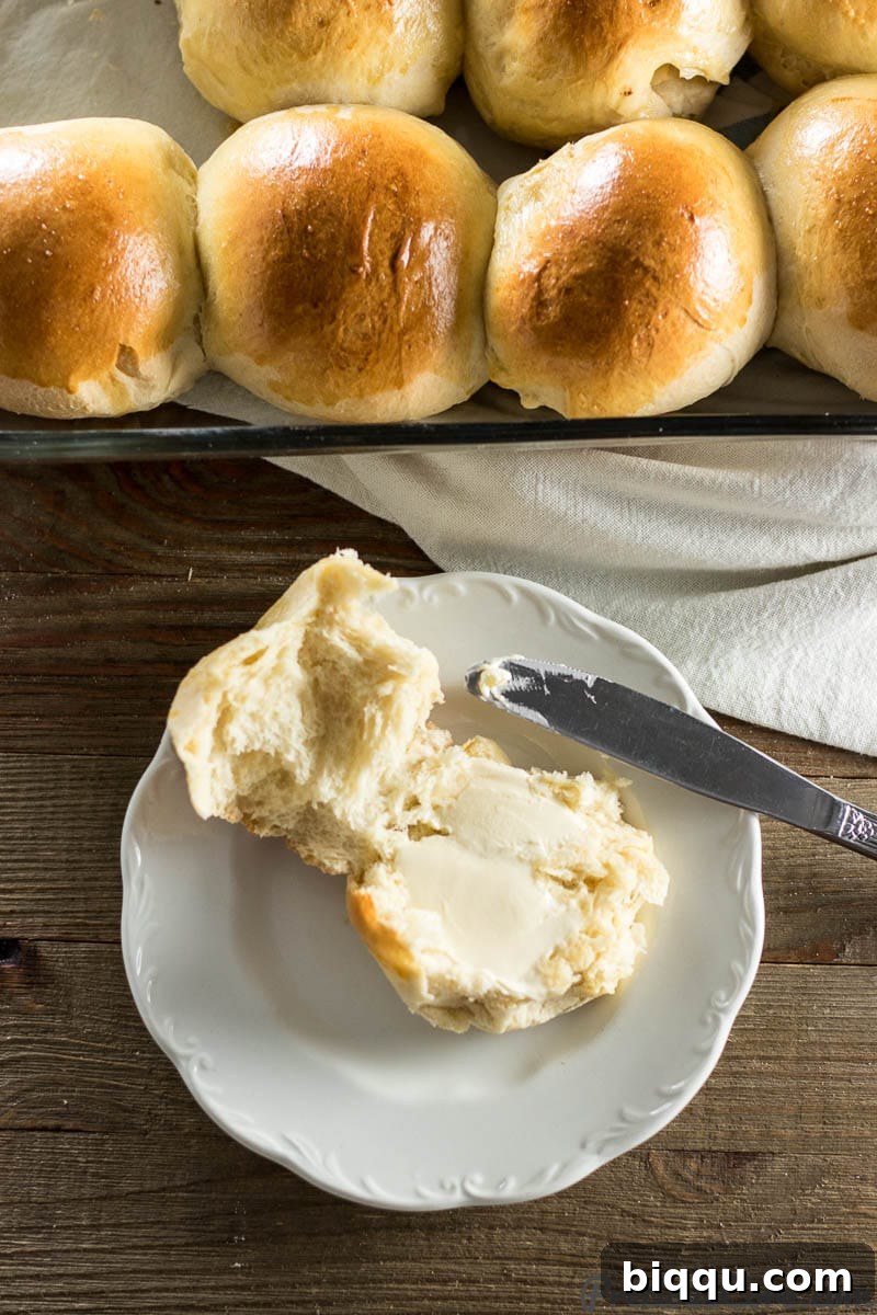 Two sweet dinner rolls on a plate, one with a generous spread of butter, highlighting their soft texture.