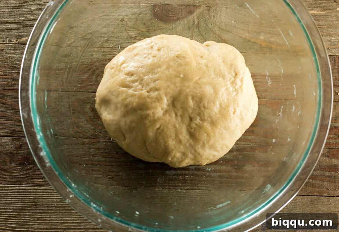 Sweet dinner roll dough in a glass bowl after mixing, appearing soft and slightly sticky.